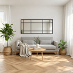 Espejo Ventana XL con marco negro y divisiones estilo industrial, instalado horizontalmente sobre un sofá gris en un living luminoso.