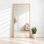 Espejo rectangular de cuerpo entero con marco de pino natural, apoyado contra una pared blanca junto a una planta.