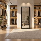 Espejo de cuerpo entero con marco negro instalado entre módulos de ropa iluminados en un vestidor con muebles de madera.