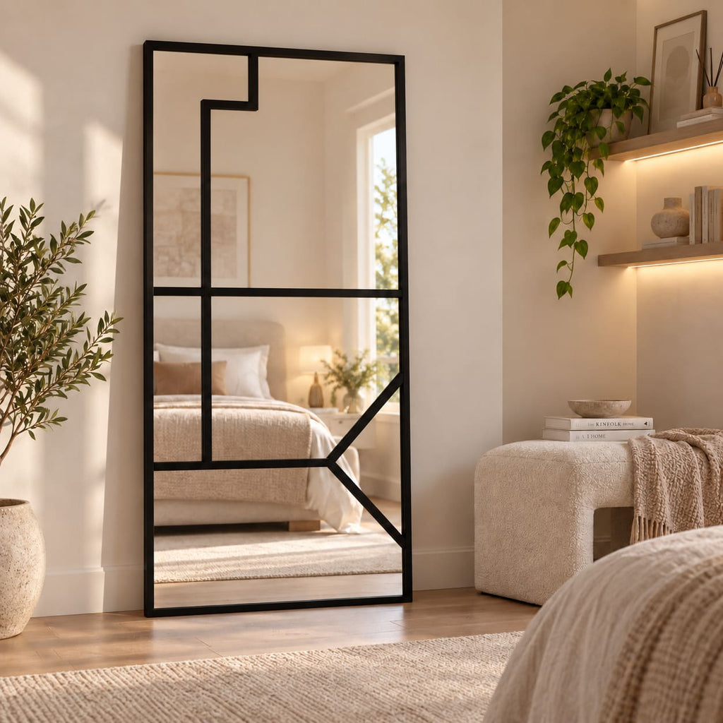 Espejo Culture rectangular con marco negro y divisiones geométricas, colocado verticalmente en un dormitorio de tonos beige