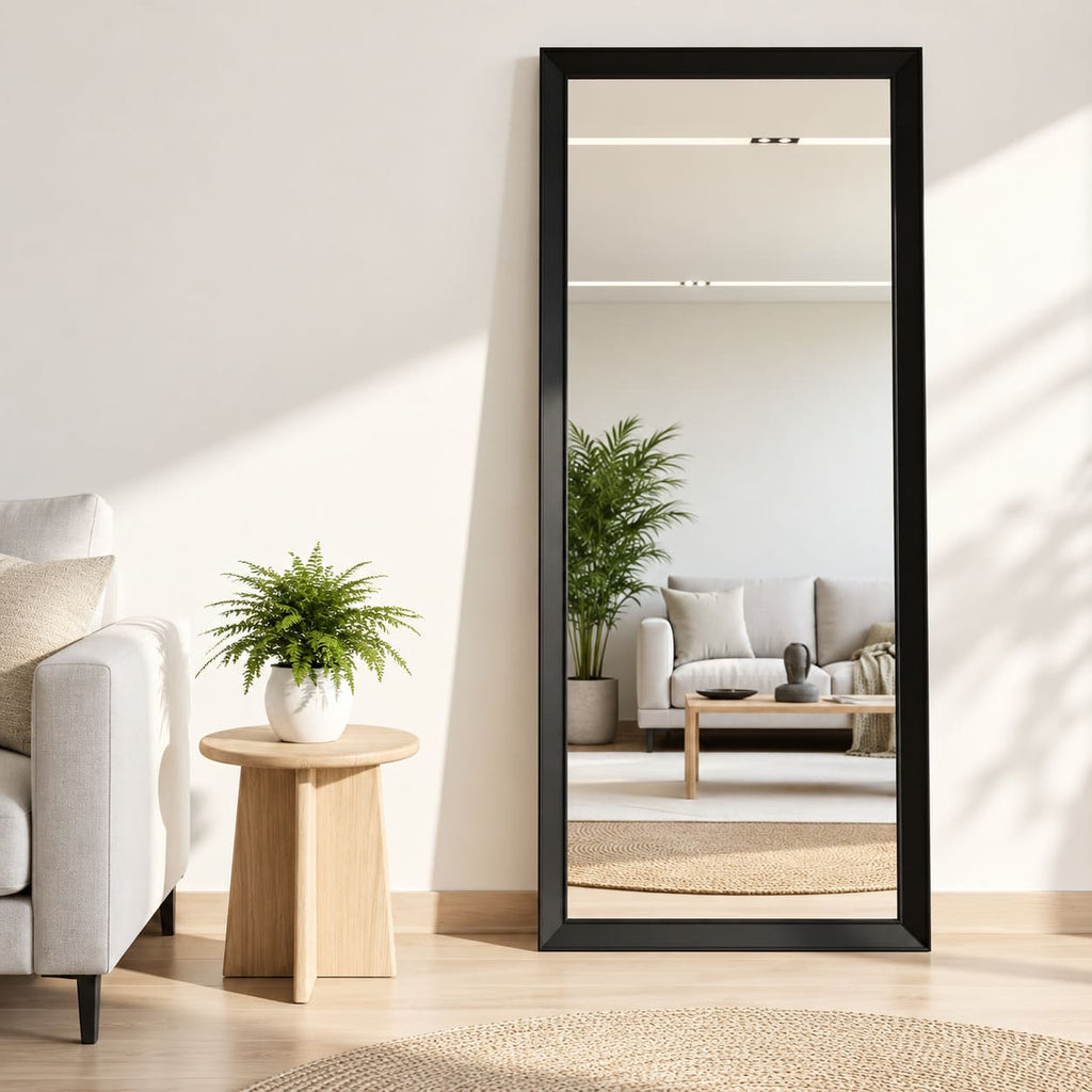 Espejo rectangular vertical con marco negro junto a una mesa auxiliar de madera y un sillón claro en un living luminoso.