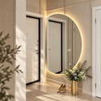 Espejo semicircular con luz LED cálida junto a la puerta de entrada y un florero dorado en el recibidor.